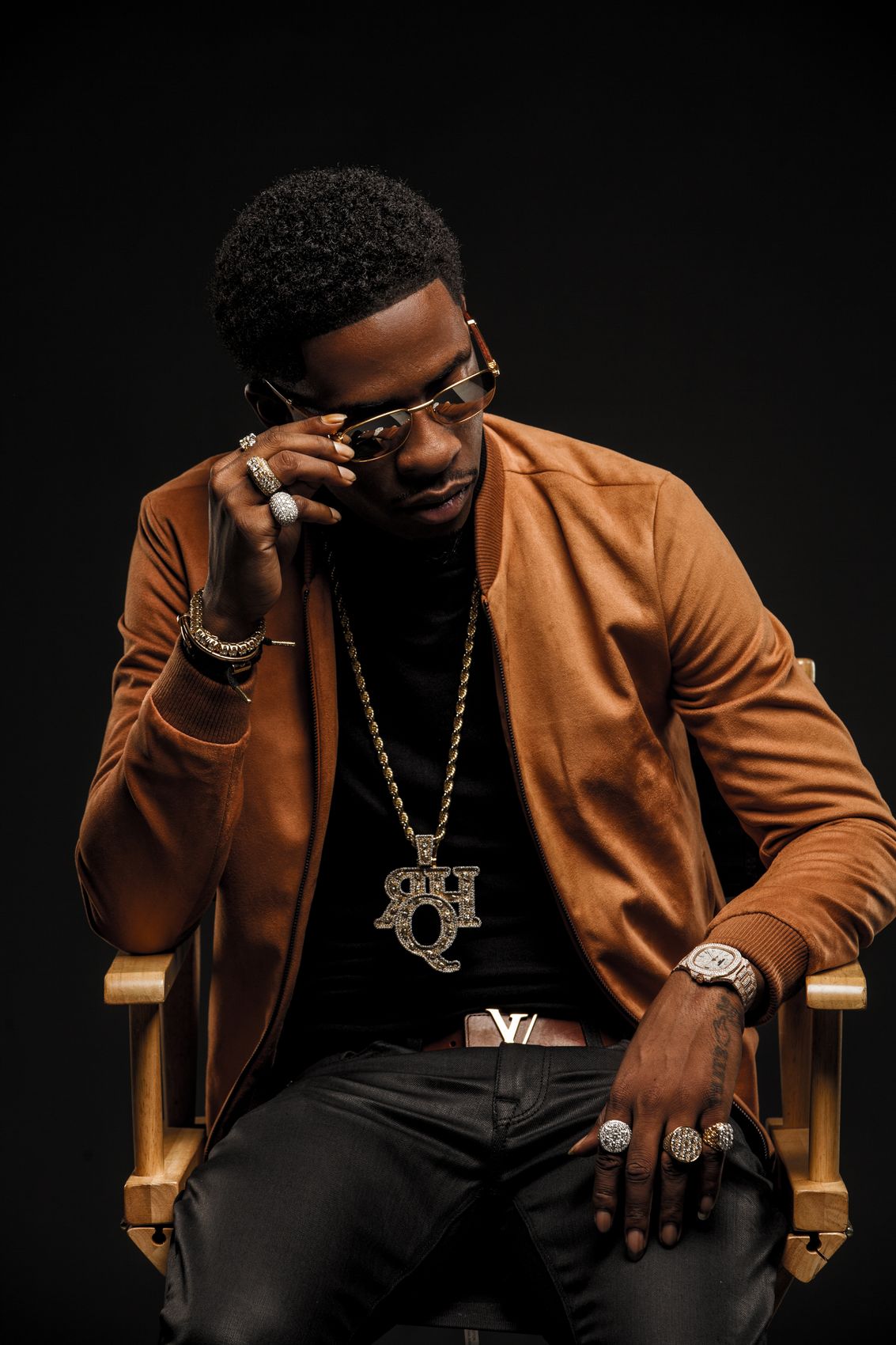 A seated editorial portrait with gold jewelry on black